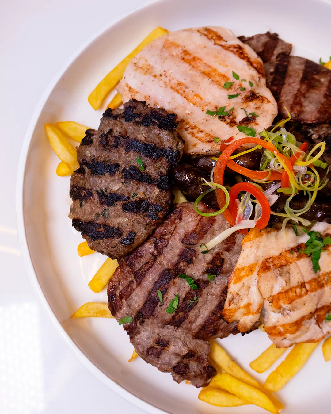 Parrilla mixta a la brasa: kafta, lomito y pollo sobre papas fritas